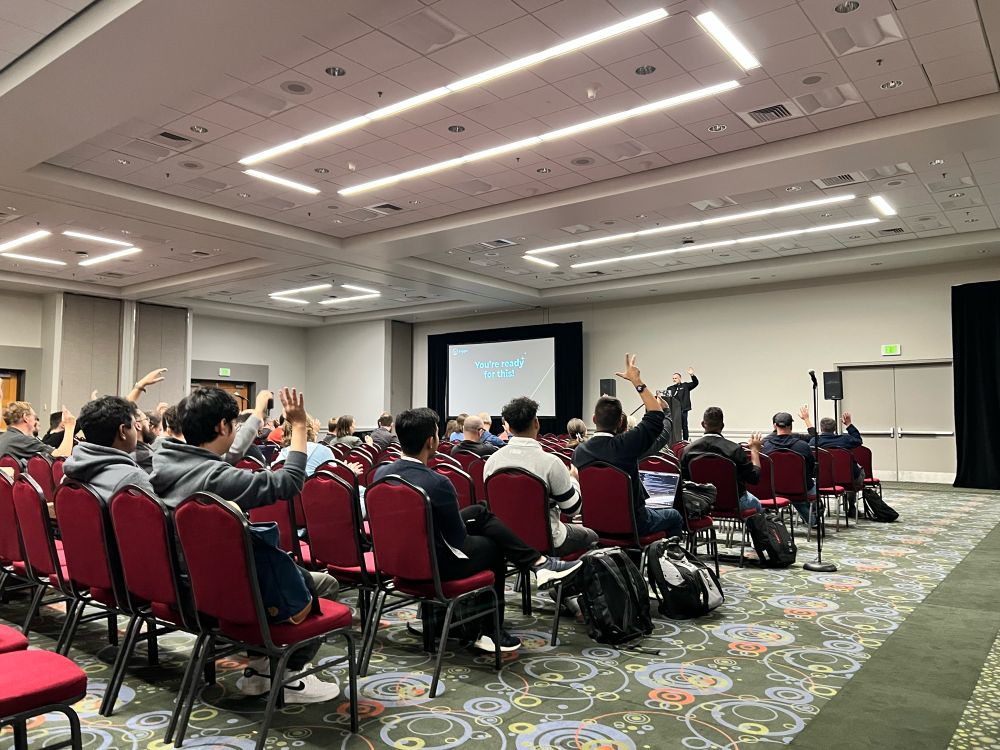 People raising their hand in a room at a presentation 
