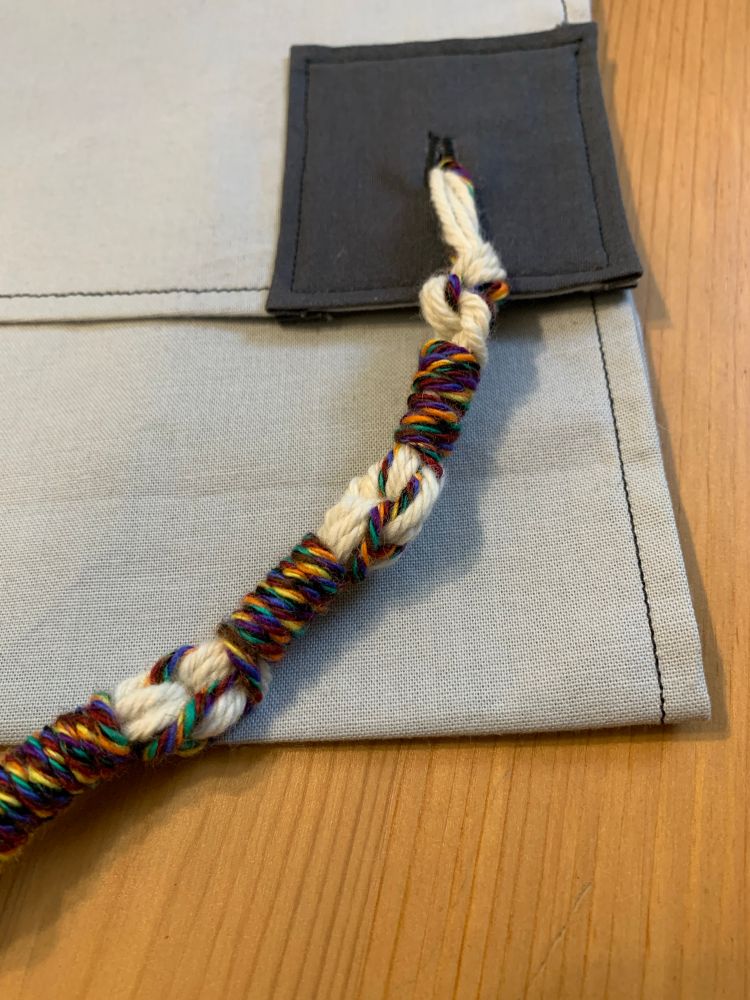 large rainbow and white sample tzitzit tied onto a corner. this close-up shows the rainbow threads wrapping around the white. 