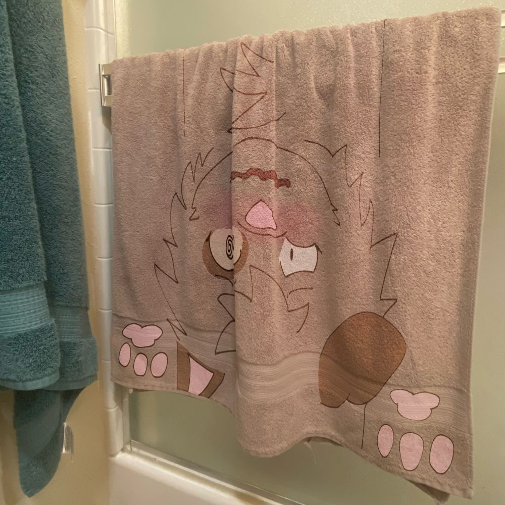a real life picture of a brown towel with my fursona, a brown dog-fox creature, drawn over it as if it was flattened