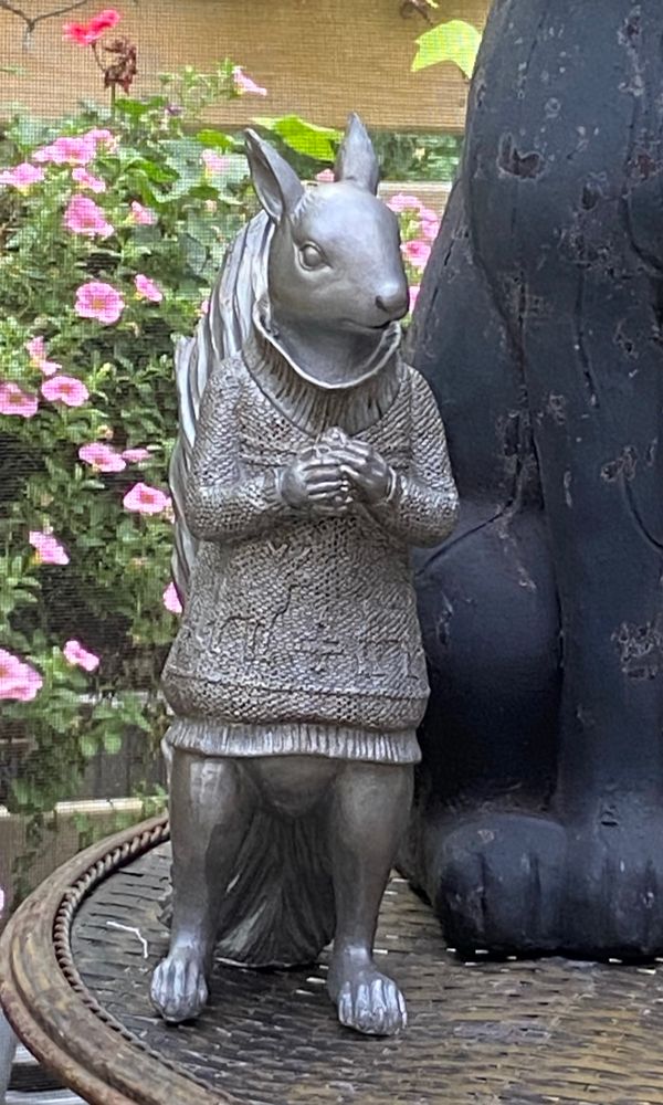 a squirrel statue in a knit sweater standing with its hands clasped
