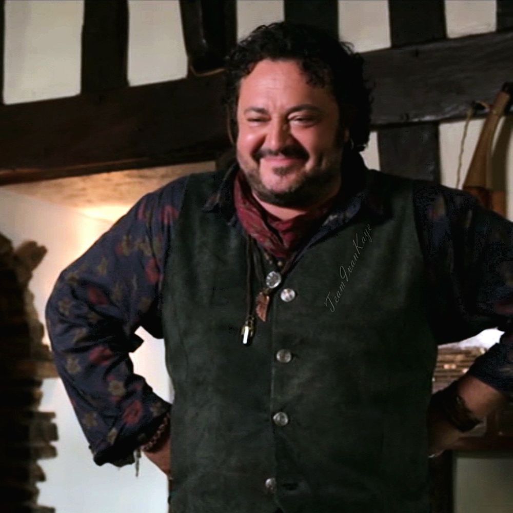 Actor Ivan Kaye as Mick Sturrock in the BBC series The Coroner with a broad smile, standing with his hands on his hips.