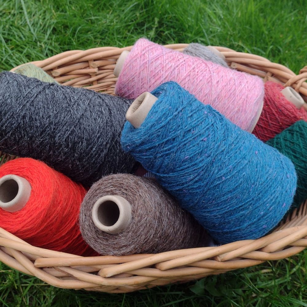 A basket of New Lanark Wool yarn in various colours on cones.