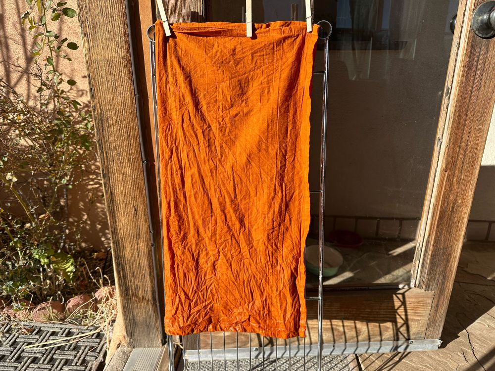 A pumpkin orange colored tea towel is drying on a rack in a doorway