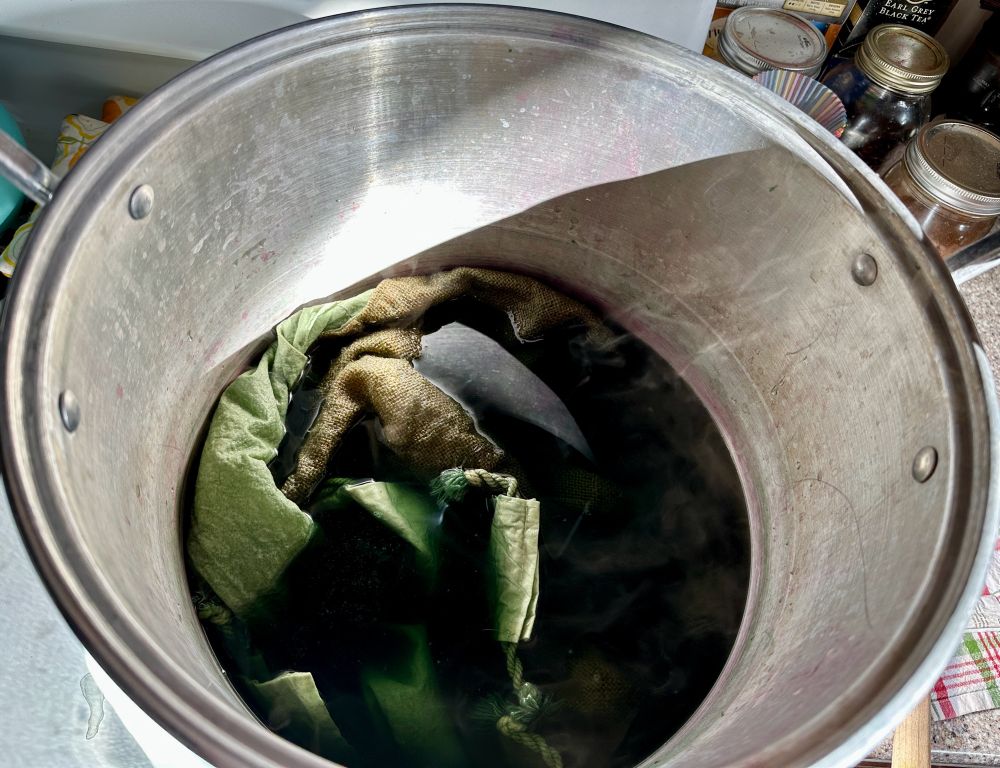 A large aluminum pot with green liquid and greenish fabric in it