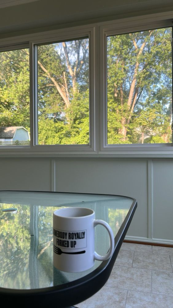 picture of a coffee cup on a table, with trees and a blue sky in the background. 
