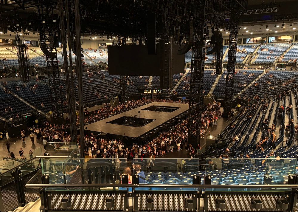 3/4 empty Rod Lave Arena set up for the Billie Eilish concert. There’s a figure 8 stage on the concert floor with people milling around, waiting for the show to start. 