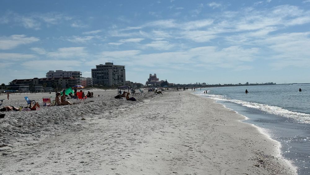 Looking south along the shoreline of St Pete beach with sunbathers and hotels in the distance 