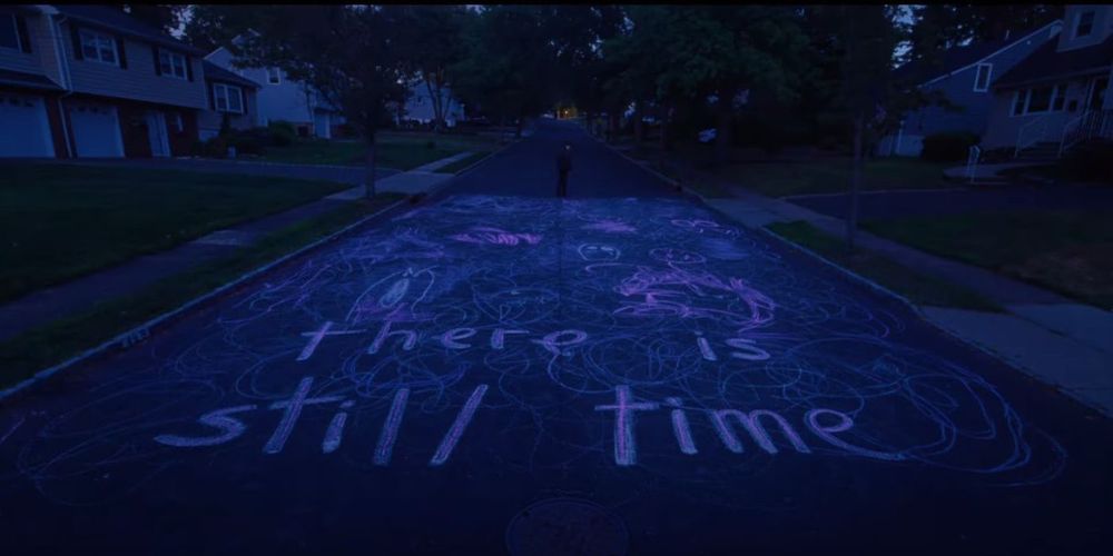 screenshot from the movie "i saw the tv glow" showing a road with chalk art that says "there is still time"