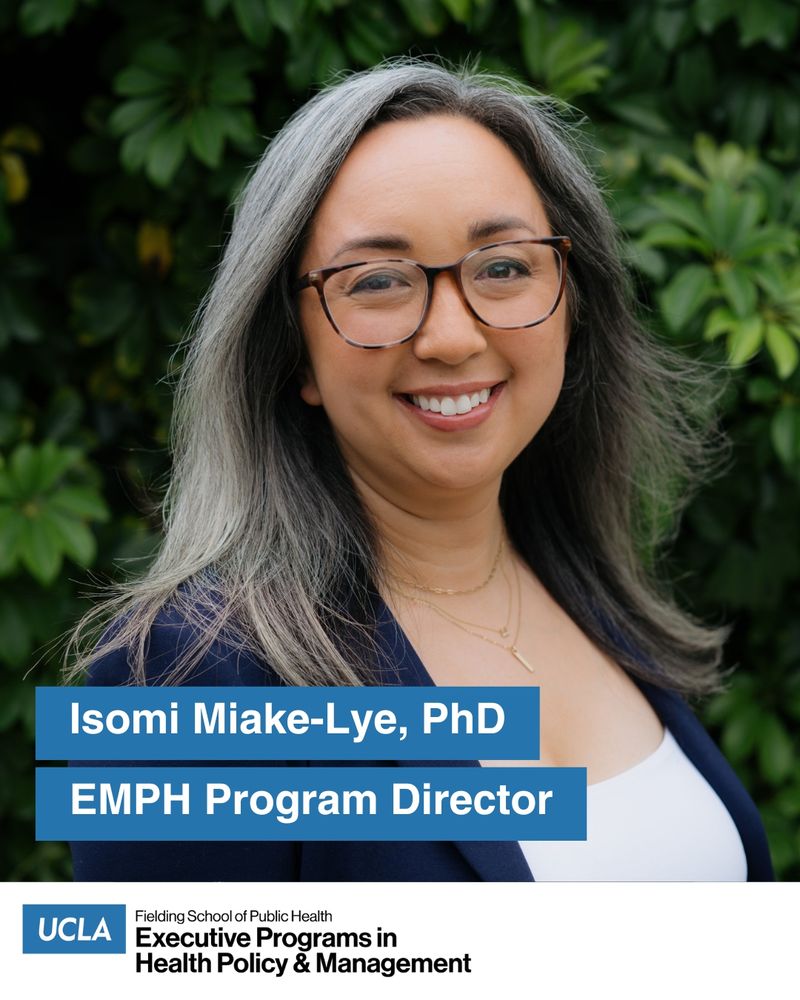 Dr. Isomi Miake-Lye stands outside in front of a green leafed shrub. She wears a navy blue blazer over a white top.