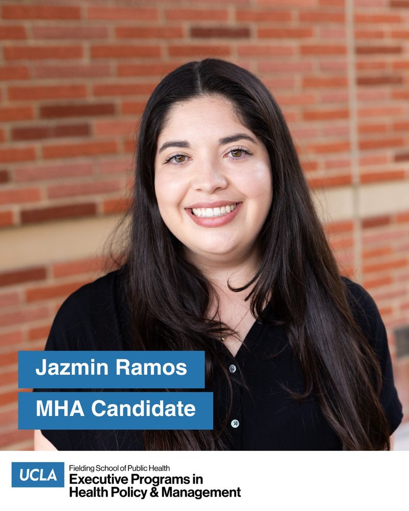 UCLA MHA student Jazmin Ramos stands outside in front of a red brick wall on the UCLA Campus. She looks straight at the camera, wearing a black shirt. She has long dark straight hair.