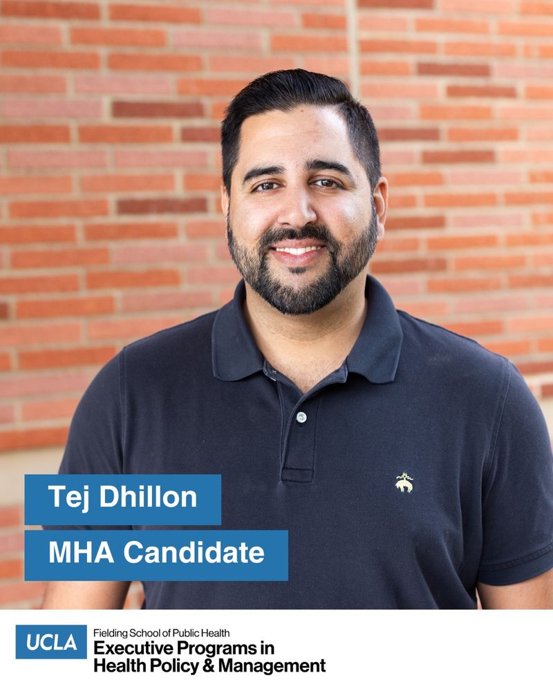 UCLA MHA candidate Tej Dhillon stands outside in front of a red brick wall on the UCLA campus. He wears a navy blue short sleeve collared shirt