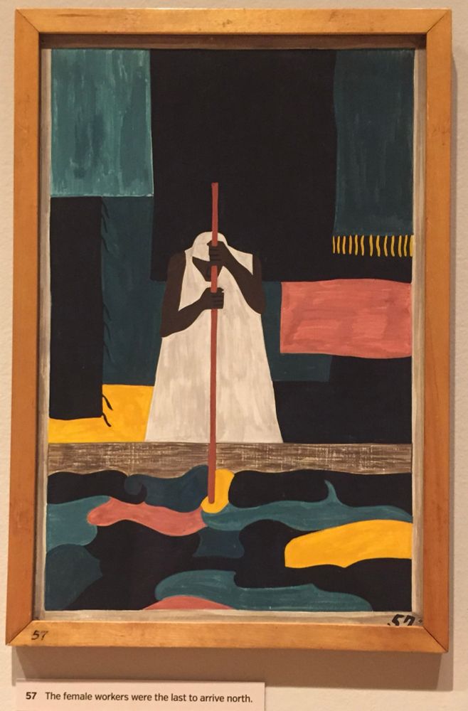 Painting by Jacob Lawrence depicts a black laundress in a long, white, sleeveless dress and a white head scarf. She is stirring clothes in a big vat of green water with a thin red pole held vertically in front of her face which is cast down. Painting is no. 57 in his series of panels depicting the great migration of former slaves. Caption: ‘The female workers were the last to arrive north.’ Phillips Collection, Washington, DC (September 2018) 