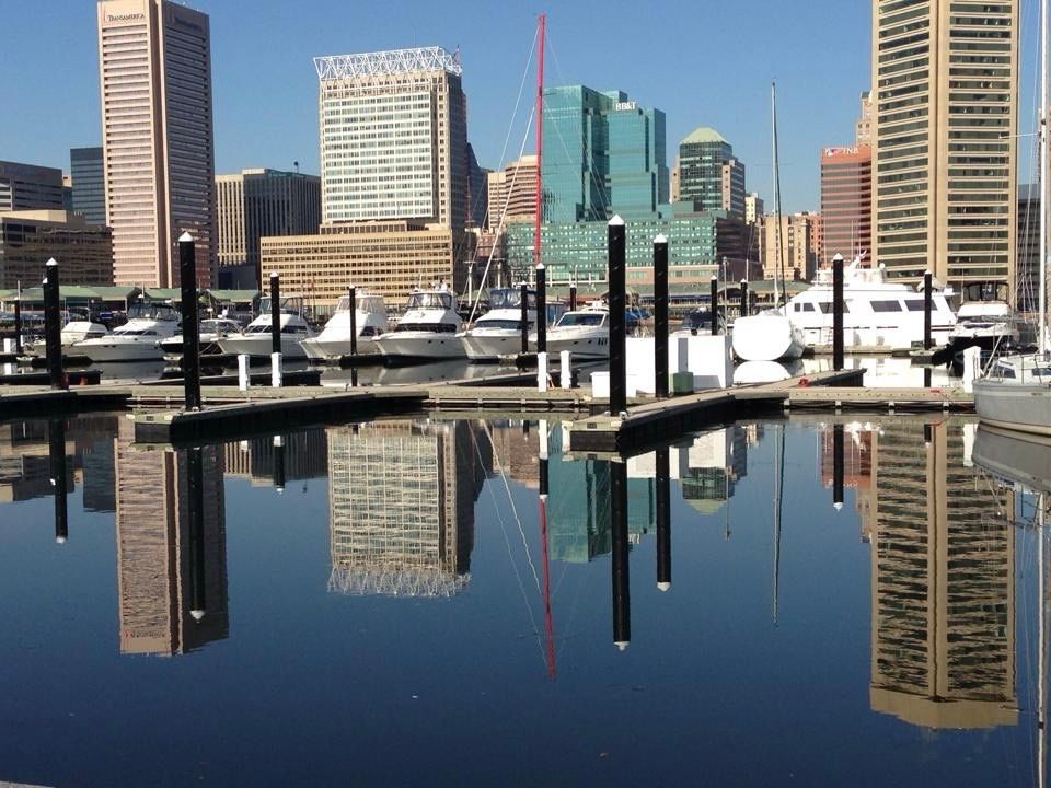 Skyscrapers are mirrored in the still surface of Baltimore’s inner harbor. A line of white yachts tied up to a wharf stretches between the mirrored image of buildings. (July 2014)