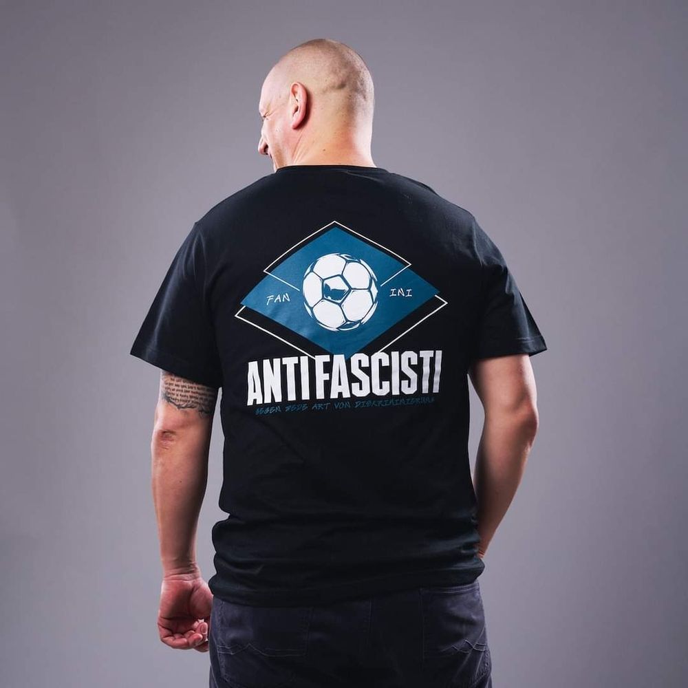 Ein Mann trägt ein dunkles Shirt. Auf dem Rücken sind der Print Antifascisti und ein Fußball zu sehen.