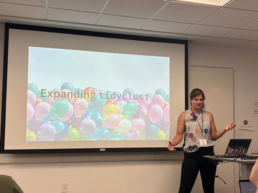 Kelly stands in front of a alide that reads "expanding tidyclust"