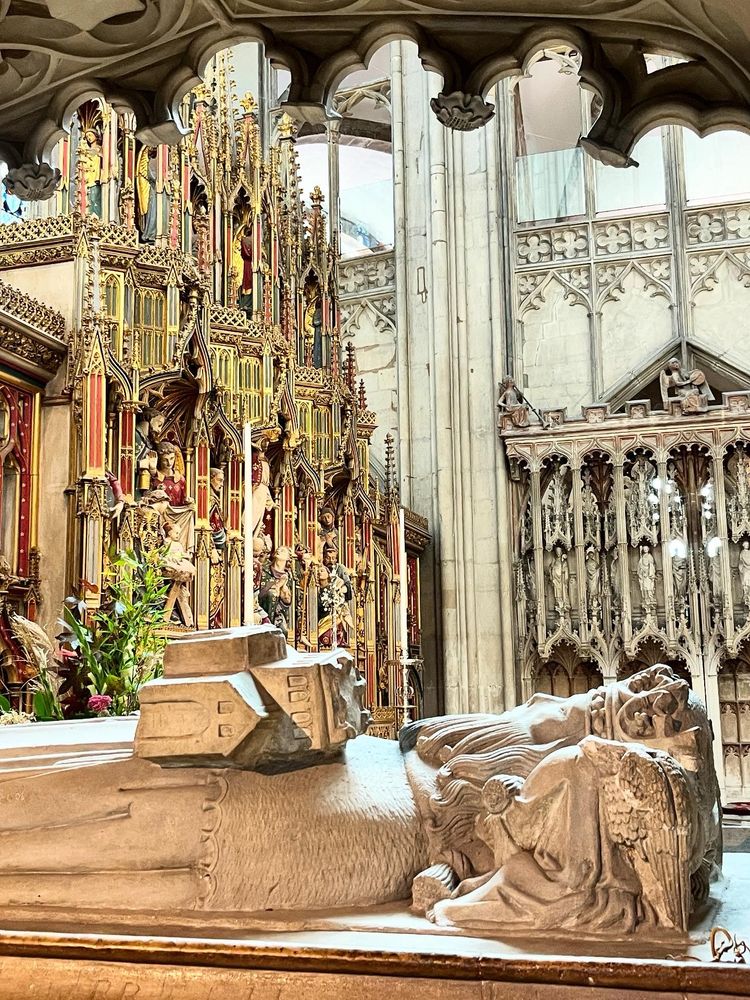 A picture of a statue lying down, behind it a window opens up onto a cathedral organ