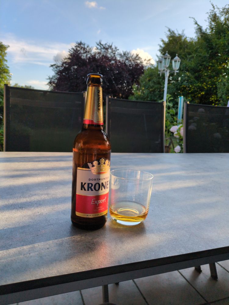 Flasche Kronen Export und Whisky tumbler auf Gartentisch, Blauer Himmel.