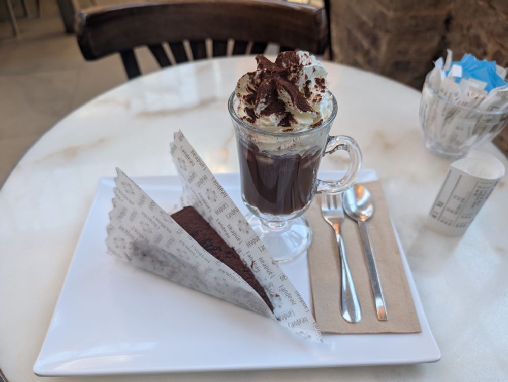 A chocolate cake in wrapping with a hot chocolate and cream 