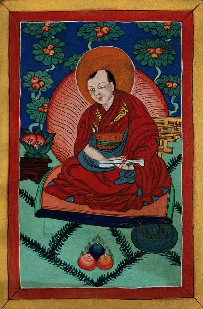 A Tibetan-style painting of a Buddhist monk or spiritual teacher, seated cross-legged on a cushion. He wears red and gold robes, has a halo behind his head, and holds a folded manuscript. The background features lush blue-green foliage and red flowers, with symbolic offerings at his feet.