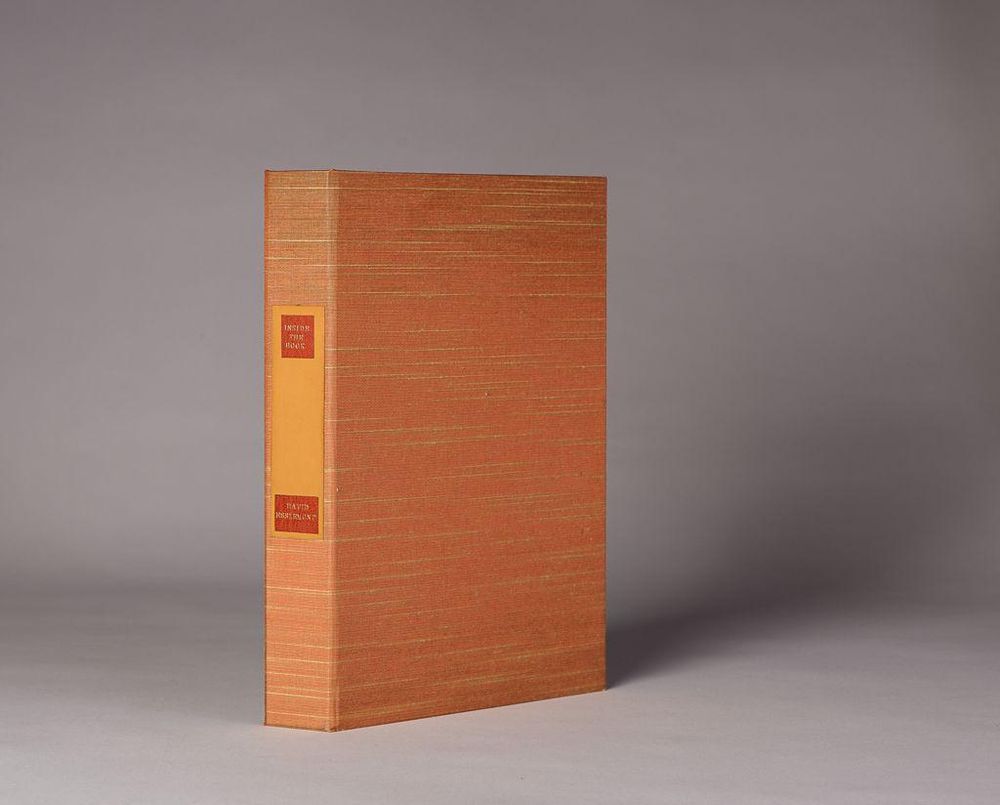 A photo of Inside the Book by Don Etherington, featuring a rust-orange woven cloth cover with subtle horizontal lines. A tan label with red blocks of text is affixed to the spine. The book is upright and slightly angled against a neutral gray background.