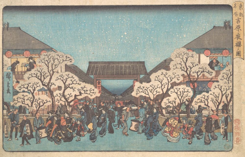 A vibrant 19th-century Japanese woodblock print depicting a lively nighttime cherry blossom scene in Yoshiwara. The print shows crowds of people walking along a bustling street lined with blooming cherry trees, lantern-lit buildings, and elevated teahouses. Geishas in elaborate kimonos, merchants, and townspeople fill the scene, framed by symmetrical architecture and a large gate in the distance beneath a star-speckled sky.