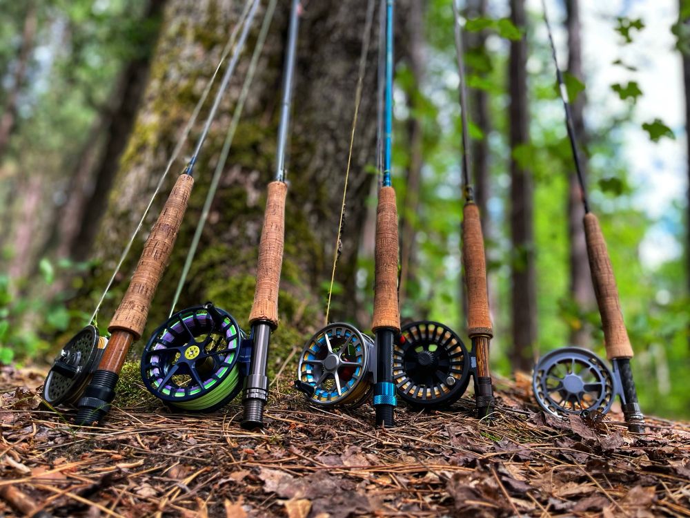 Fly fishing rods and reels leaned up against a tree. 
