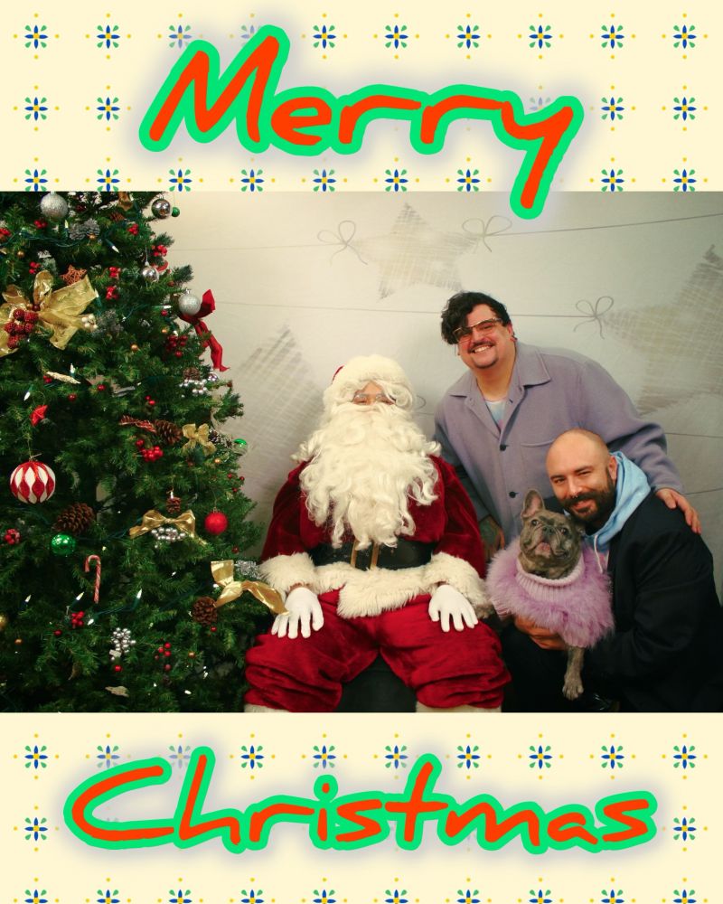Christmas photo of two men with their dog, posing with a Santa Claus in front of a decorated Christmas tree. One man is holding the dog, which is wearing a purple sweater. Both men and Santa are smiling. There's a festive border around the image and the words "Merry Christmas" are written in red and green at the top and bottom.