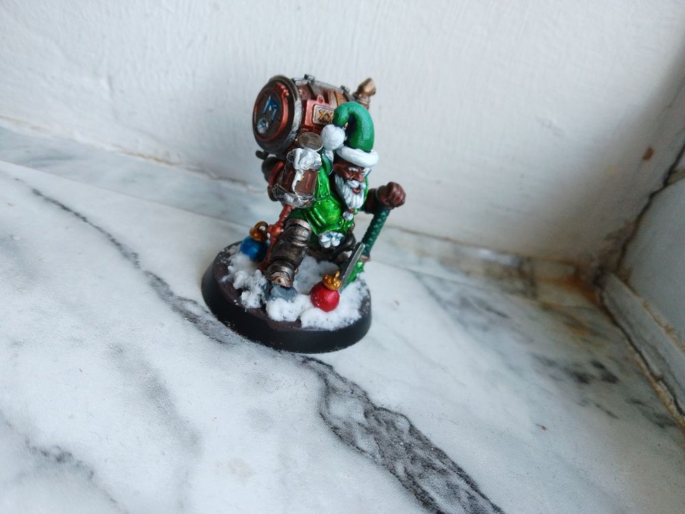 A green Christmas dwarf brandishing a pint in the snow