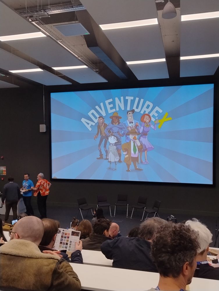 A lecture hall showing the AdventureX logo on screen.