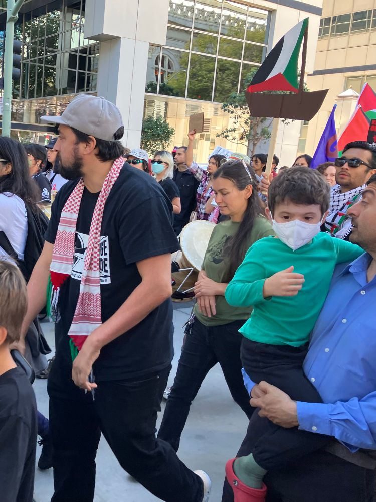 Protestors marching wearing keffiyehs, with a man in the foreground carrying a young boy in his arms 