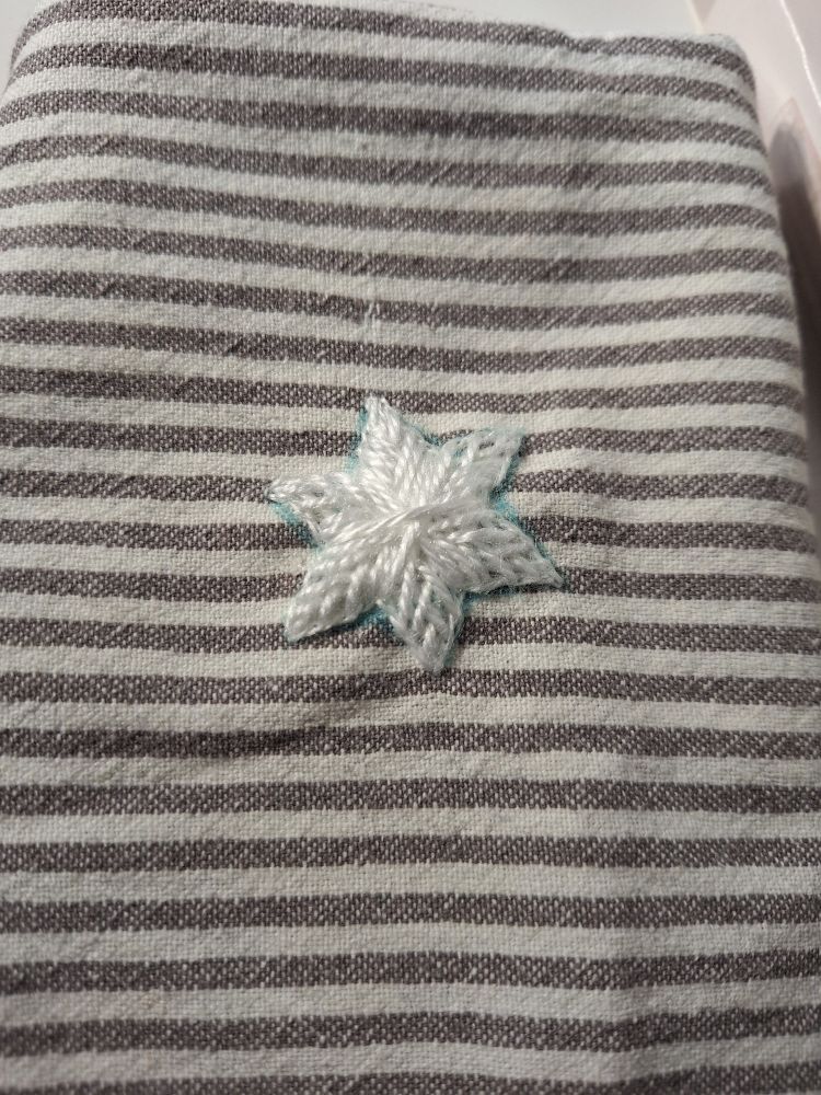 A white dishtowel with thin grey stripes. In the middle is a white star. It has 6 points and was used to cover a hole. 