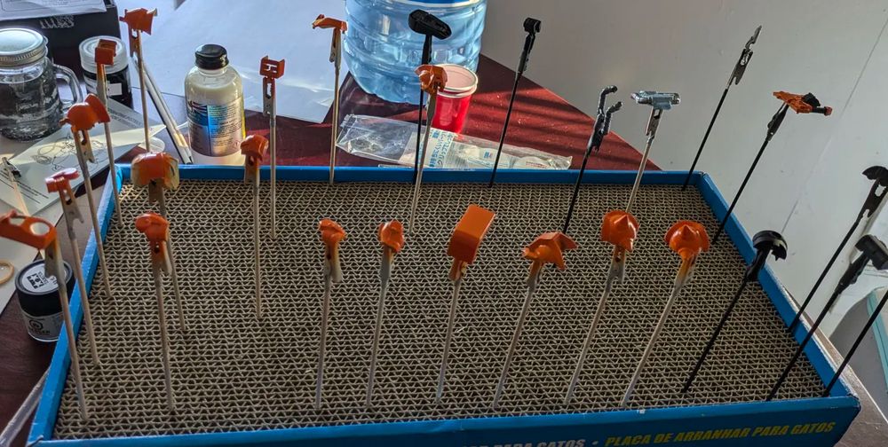 A bunch of painted gunpla parts on paint sticks.