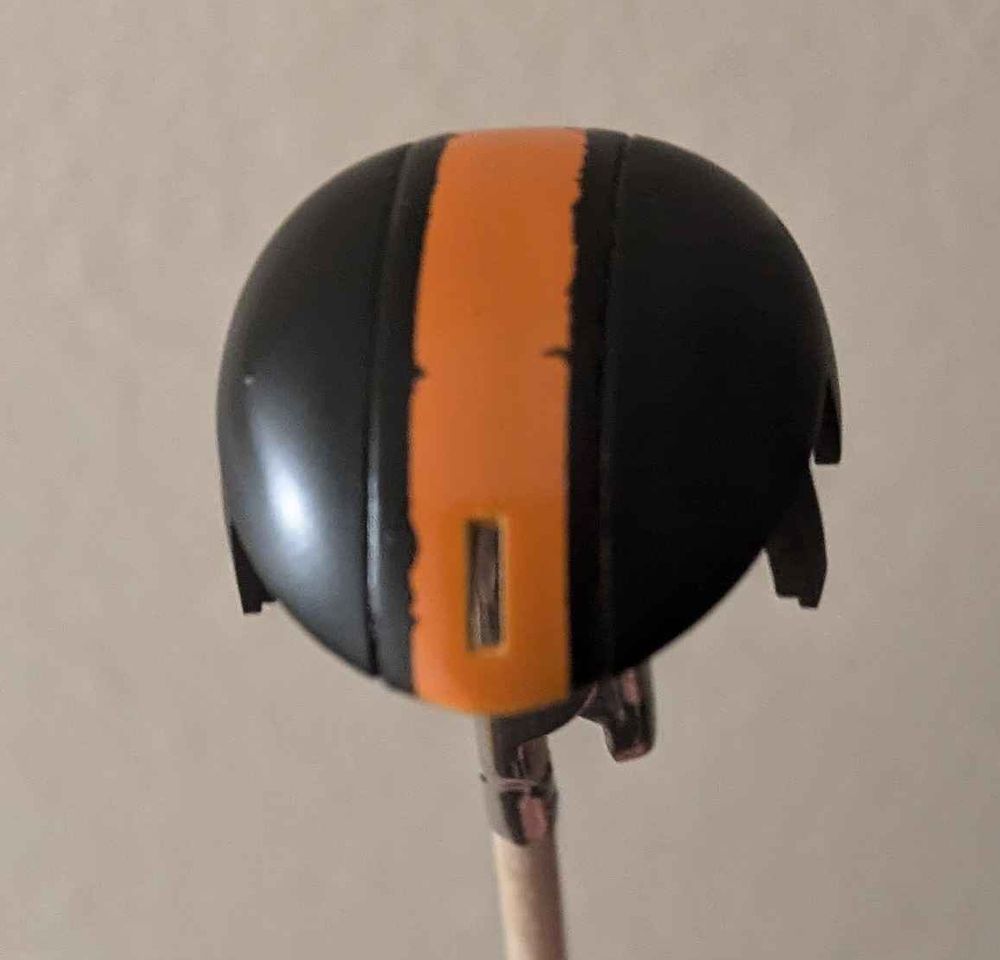The head top piece of the SDCS Zaku-II gunpla painted black with an orange stripe down the middle, and some black paint bleeding on the edges.