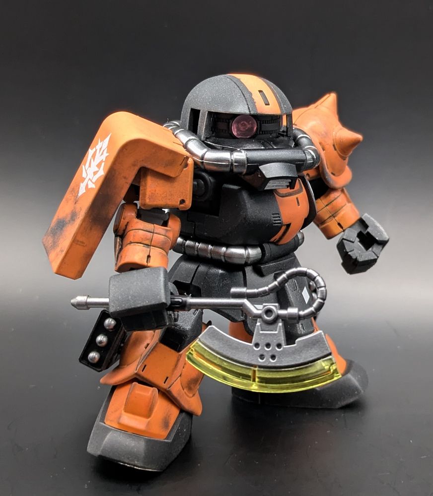 The SD Cross Silhouette Zaku-II gunpla model kit from the Gundam series. It is custom painted orange/black/chrome and is holding its heat hawk.