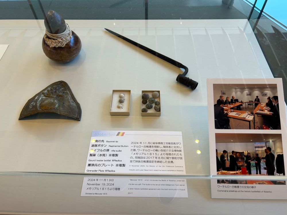ワーテルロー古戦場から贈られたフランス軍の銃剣、ボタン、銃弾、水筒（レプリカ）、擲弾兵の帽章（レプリカ）の展示写真。