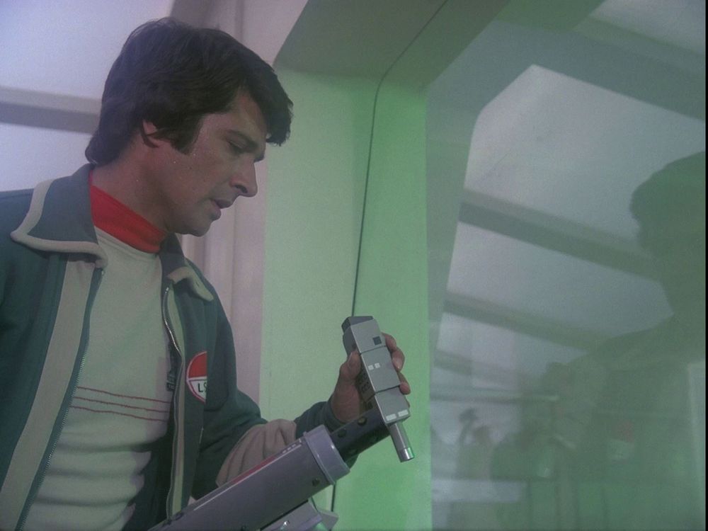 A character from the TV show, Space: 1999 uses his commlock communicator device, and handheld video, two-way communicator.
