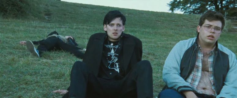 A still from the film The World’s End showing Gary King, a young man with a black mullet, a Sisters of Mercy t-shirt and a black coat and trousers, sitting with his friends, wasted after a night out, watching the sun come up over the small town they live in.