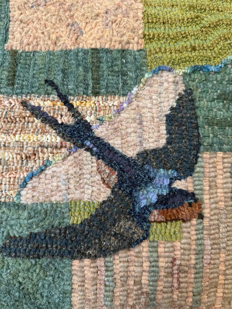 Fiber art of a barn swallow flying above farm fields.  Medium is hooked wool and silk.  
