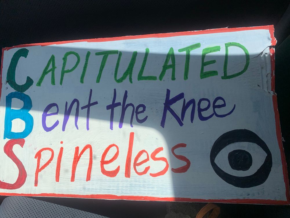 Sign reading Capitulated. Bent the knee. Spineless, in colorful lettering 