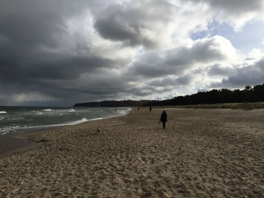 Dark sky over a beach - sea visible, few people walking