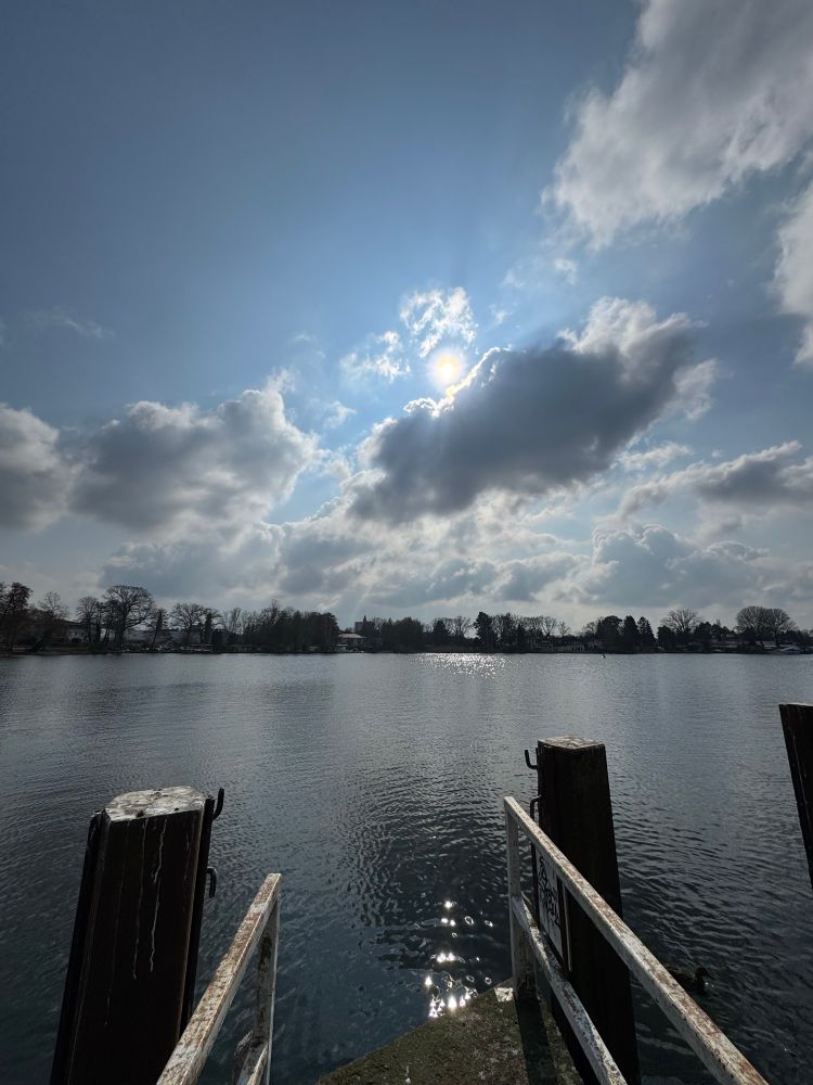 a pier leading on a lake, cloudy sky pale sun 
