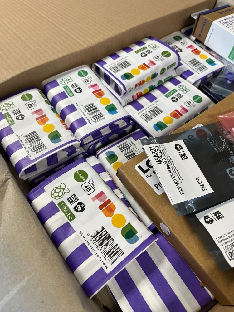 Large box of Pimoroni Pibow cases individually wrapped in purple and white striped bags.
