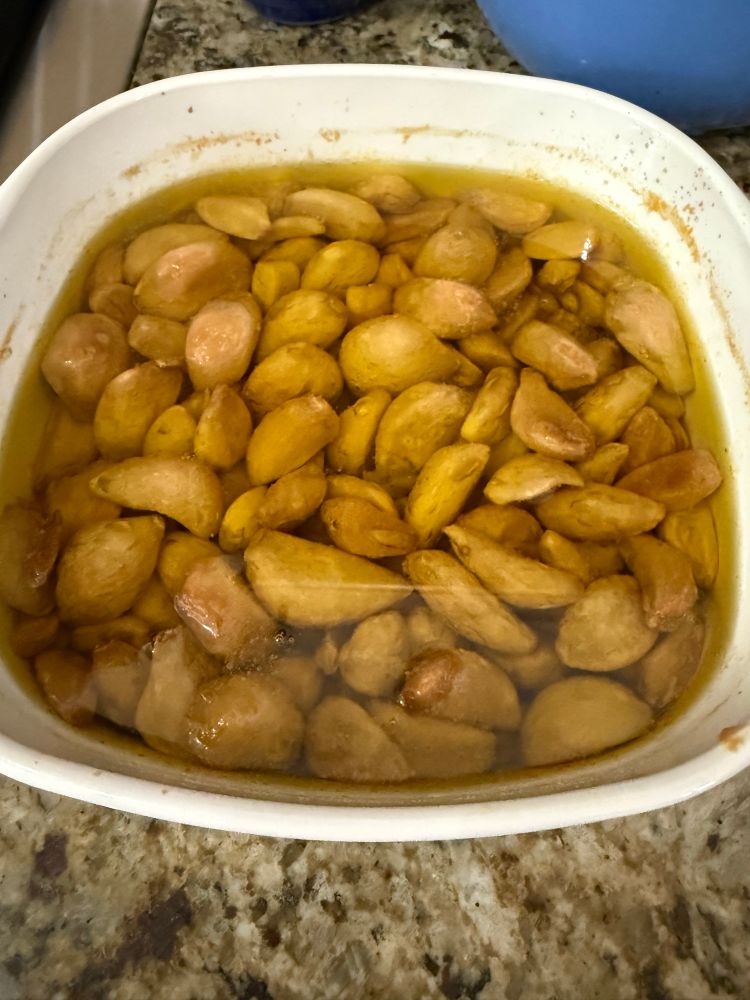 White Baking dish full of brown roasted garlic cloves and olive oil
