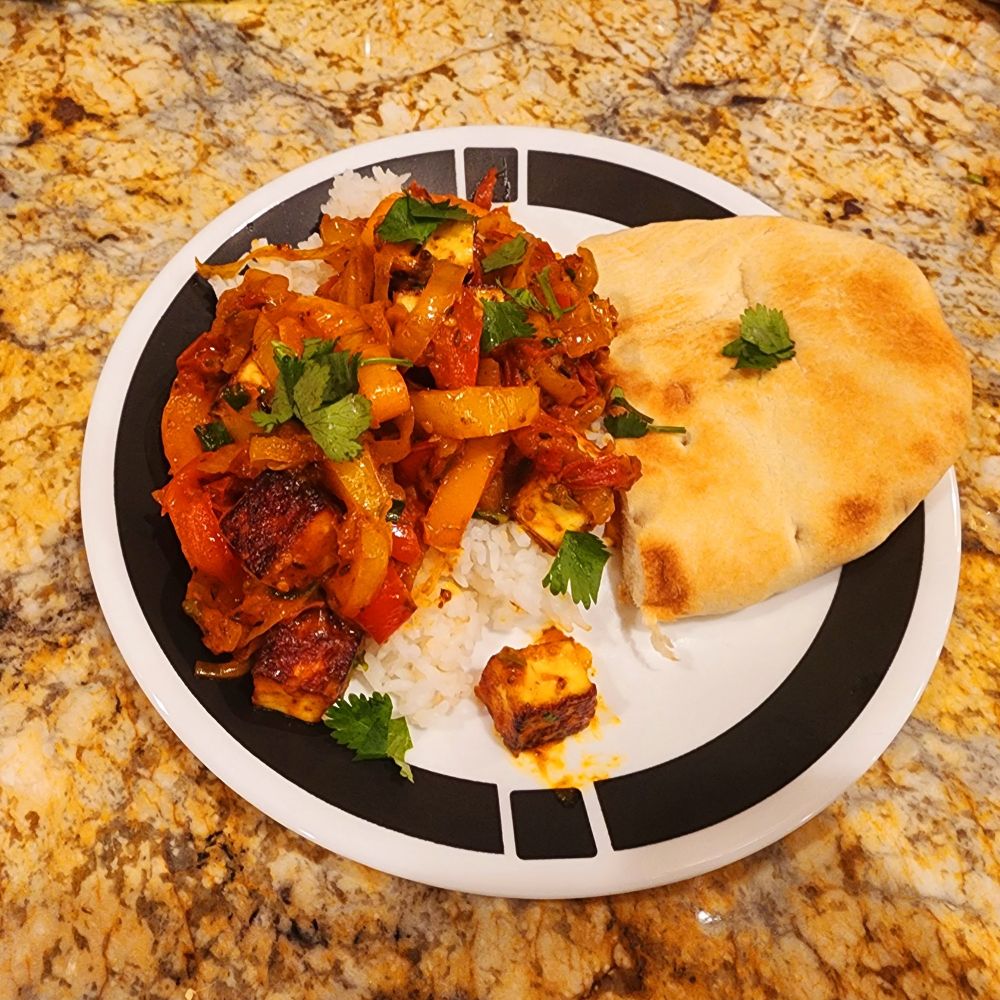 A plate of red pepper curry with rice and flat bread 
