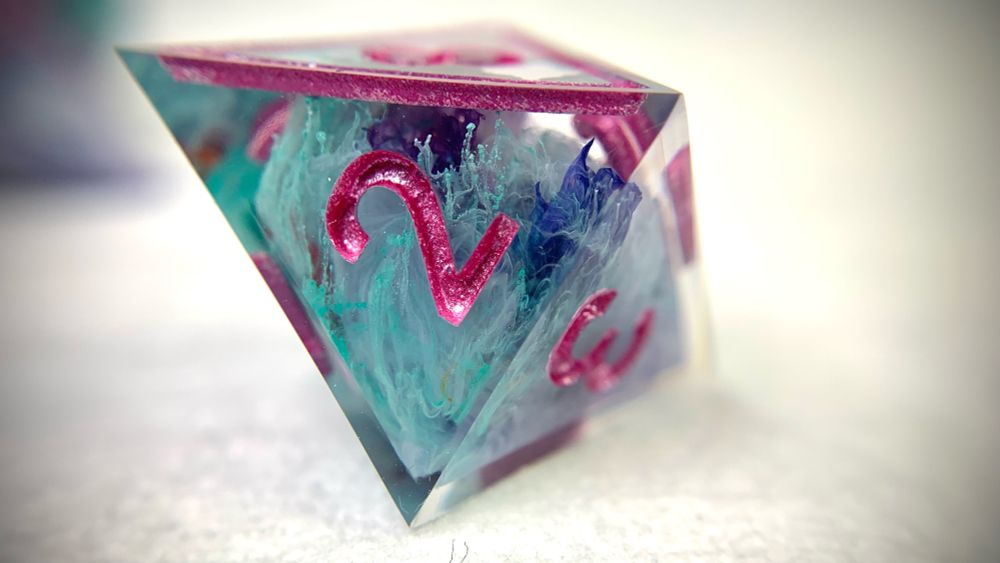 A d8 with vibrant teals, pinks, and oranges. The colours have a petri vibe, stringing out within the dice. 