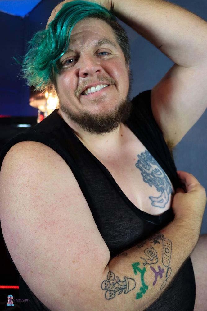 Transmasc with green hair and tattoos showing off armpit hair