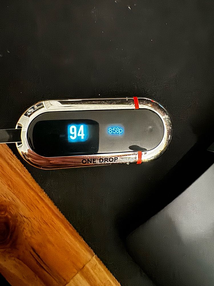 One drop blood glucometer showing a result of 94 mg/dL at 8:58pm CT on a black mousepad and wood background. Due to daylight savings time differences, this was actually done at 7:58pm.