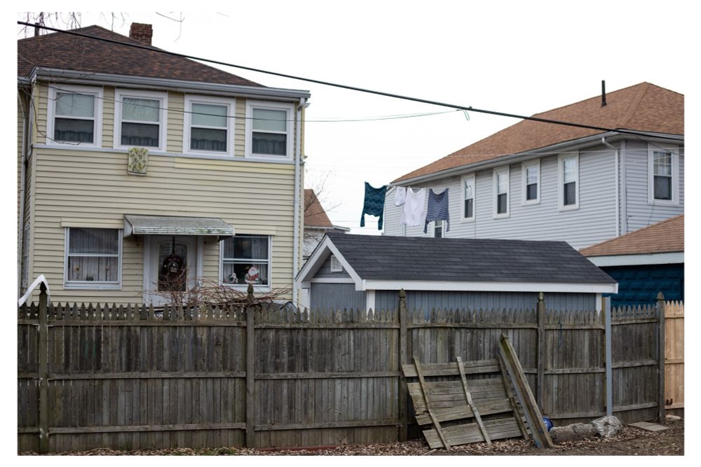 A color photo of laundry hanging on a line in a backyard of a home that is behind a fence along a bike path in Malden. 

Malden, MA. 2020.