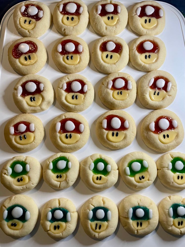 Rows of thumbprint cookies made to look like Mario Mushrooms, red, green and blue. 