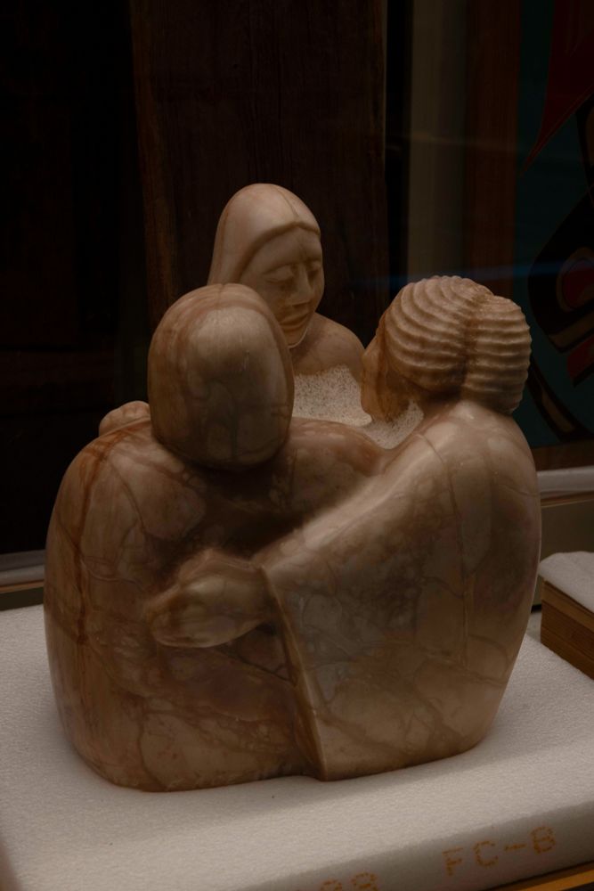 Smooth sculpture of three women holding arms in a circle